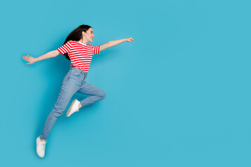 Full length photo of adorable lovely girl wear striped t-shirt jumping high rising fist empty space...
