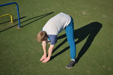 A focused young athlete dynamically performing warm-up drills and stretches outdoors. Clad in...
