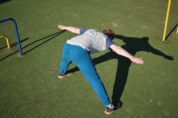 A focused young athlete dynamically performing warm-up drills and stretches outdoors. Clad in...