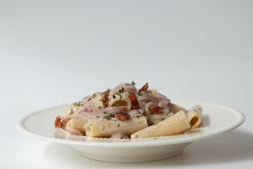 Traditional Italian food concept, Rigatoni Carbonara topped with Ham and Parmesan on white background