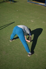 A focused young athlete dynamically performing warm-up drills and stretches outdoors. Clad in...