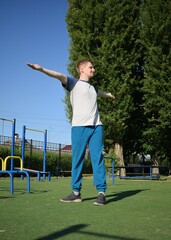A focused young athlete dynamically performing warm-up drills and stretches outdoors. Clad in...