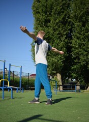 A focused young athlete dynamically performing warm-up drills and stretches outdoors. Clad in...