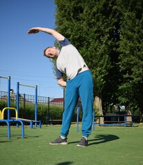 A focused young athlete dynamically performing warm-up drills and stretches outdoors. Clad in...