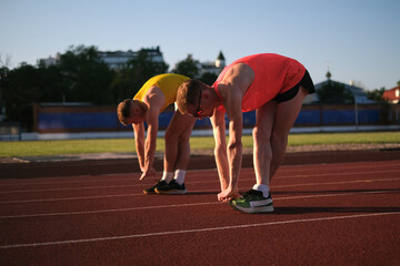 Two runners do warm-up bending exercises at the stadium before the race