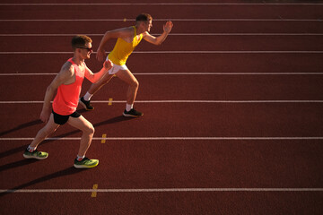 Two athletes running in a stadium at sunset
