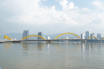 Naklejka premium A yellow bridge spans a body of water in front of a city skyline