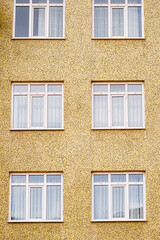 Facade of a yellow textured building with six white framed windows arranged in two columns and three rows.