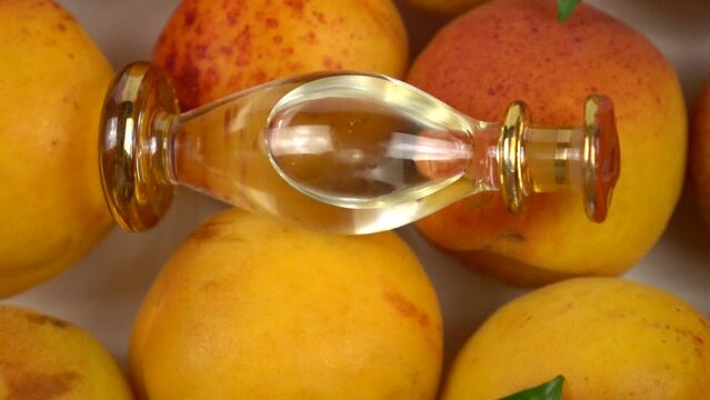 Glass bottle with apricot kernel oil placed on the ripe fresh apricot fruit, background, slow motion