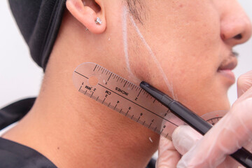 An esthetician marking lines on a man's jaw area as a guide for jawline filler procedure. Using a goniometer as a guide. Shaping a more squarish and manlier jawline.