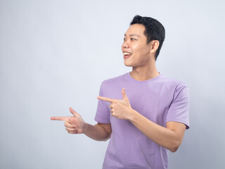 Young Asian man in a lavender t-shirt pointing with both hands and looking excitedly in the...