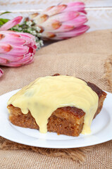 Traditional South African Malva pudding . one serving with custard on a plate with burlap and copy...