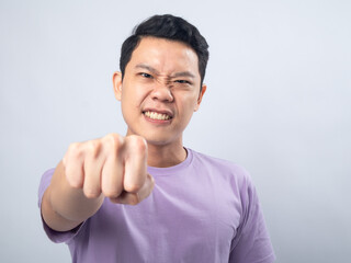 Young Asian man in a lavender t-shirt with an angry expression, clenching his fist and showing aggression. Studio shot on a plain background, highlighting his intense emotion and casual fashion.