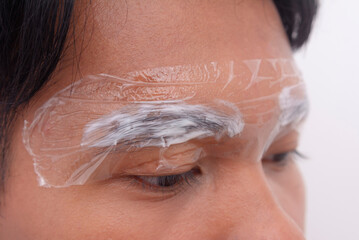 Close-up of a man's eyebrows with numbing cream wrapped in clear plastic, preparing for a...