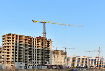 View of a large construction site with buildings under construction and multi-storey residential homes.Tower cranes in action on blue sky background. Housing renovation concept. Crane during formworks