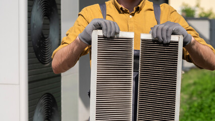Man with gloves holding two clogged air filters from a home ventilation system.