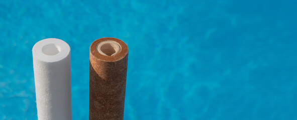 Two water filter cartridges, one clean and one dirty, against a swimming pool backdrop. Wide shot