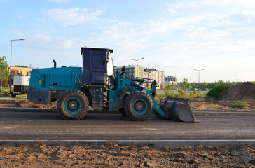 Obraz premium Wheel loader with a bucket on the road construction. Construction site with heavy machinery on road construction. Civil engineering. Heavy machinery for loading and unloading works on roadworks.