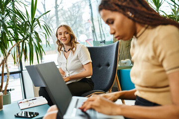 Two women with laptops working together at a table in a modern coworking space, engaged in a startup team meeting.