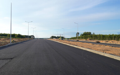 Fototapeta premium Asphalt road after laying asphalt. New asphalt road renovation. Road construction. Paved highway. Black tarmac road after rebuilding, repair, renovation. Black tarmac rebuilding. Street Asphalting.