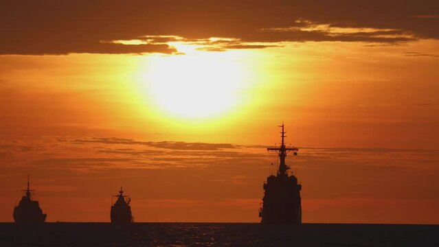 Time lapse silhouette of three warships at sea at sunset