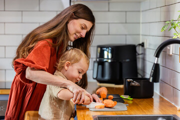 happy mum with two year old son cooking together chopping vegetables in kitchen