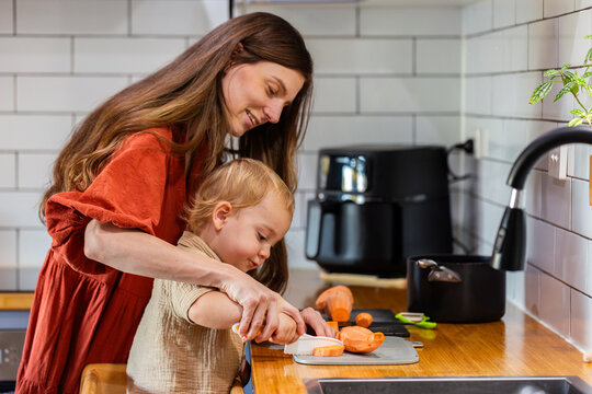 happy mum with two year old son cooking together chopping vegetables in kitchen - Powered by Adobe