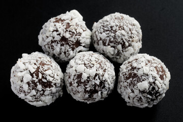 Five round spherical chocolates sprinkled with coconut flakes on a dark background. Photo. Macro. Selective focus