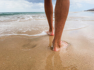 Stopy mężczyzny chodzącego po piasku i falach morskich. Mężczyzna spacerujący boso po plaży. 
