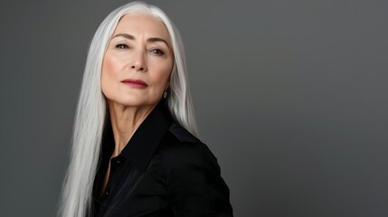 Elegant mature woman with long silver hair, wearing a black outfit. She exudes confidence and poise, set against a neutral gray background