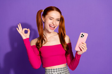 Photo of charming positive girl wear pink top winking eye showing okey chatting modern gadget...