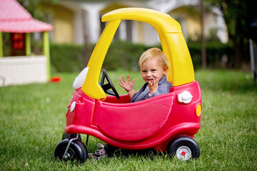 Cute toddler boy, riding big plastic red car toy in the park