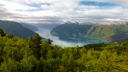 A breathtaking view of a Norwegian fjord, surrounded by lush green forests and snow-capped mountains, under a cloudy sky. Molden hike, Norway