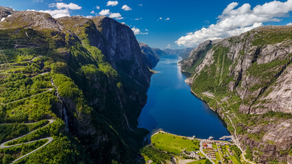 Fototapeta na wymiar A scenic aerial view of a winding road carved into the steep cliffs of a Norwegian fjord, with a picturesque village nestled at the base. Lysebotn, Lysefjorden, Norway