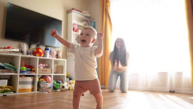 Family. The first steps to bringing your baby home. Child mother toddler family concept. Baby learns to walk indoors. A baby running on a wooden floor lifestyle with a woman.