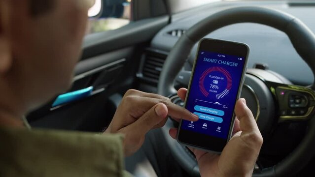 Over the shoulder view of male driver sitting in car and looking at smartphone with EV charging application on screen