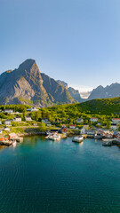 Fototapeta premium An aerial view of a peaceful harbor in Lofoten, Norway, surrounded by majestic mountains and lush green hills. Reine, Lofoten, Norway
