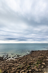 The seascape portrays a rocky shoreline under a cloudy sky, with tranquil waters, creating a serene coastal scene