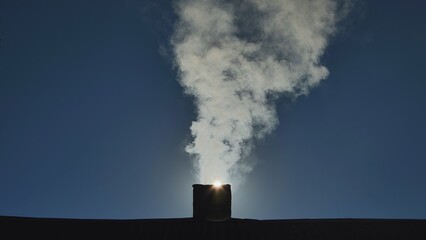 Silhouette of smoke against the sun from the chimney of a village house. © Довидович Михаил