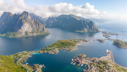 An aerial view of Reine, a picturesque village in the Lofoten Islands of Norway, showcasing the dramatic mountains, clear waters, and charming harbor. Reinebringen, Lofoten, Norway
