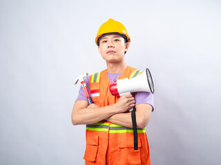 Young Asian man in an orange safety vest and yellow hard hat, holding a megaphone and shouting, isolated on a white background. The image conveys urgency, communication
