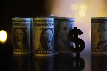 Rolls of US Dollar Bills with Dollar Sign Symbol on Dark Background with Bokeh Lights