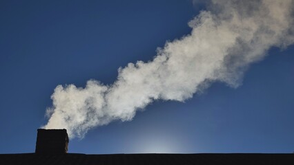 Silhouette of smoke against blue sky from the chimney of a village house.