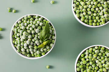 Three white bowls filled with frozen green peas on green background.