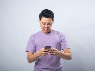 Young Asian man in a lavender t-shirt angrily shouting at his smartphone. Studio shot on a plain...