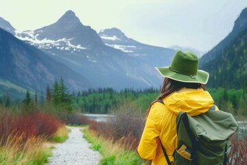girl in a yellow jacket with a backpack in a green hat looks at the mountains rear view close-up