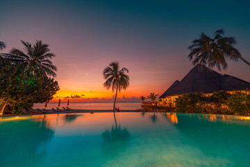 Tropical sunset over outdoor infinity pool in summer seaside resort, beach landscape. Luxury tranquil beach holiday, poolside reflection, relaxing chaise lounge romantic colorful sky, chairs umbrella