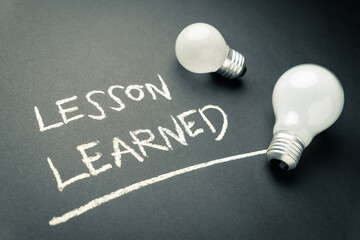 Lesson Learned topic, handwritten with chalk on the chalkboard, with small and bigger light bulbs
