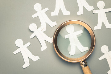 Closeup paper human dolls and magnifying glass on the table, find a talent people, recruitment,...