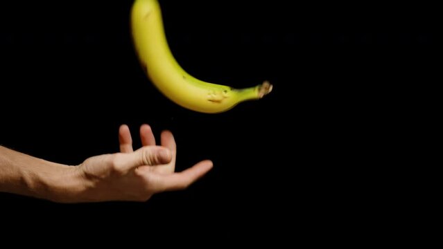 Hand Spins Banana While Tossing It in the Air, Slow Motion, Isolated on Black Background.